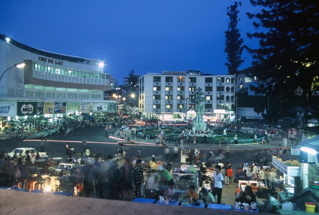 a crowd of people gathered around a street corner in a city - File:Dalat market, Vietnam.jpg