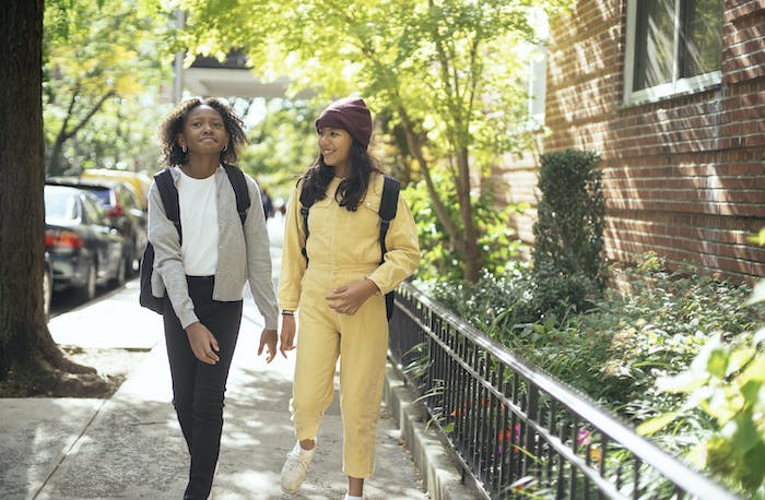 Cheerful diverse schoolkids in casual outfit speaking while strolling on an urban walkway