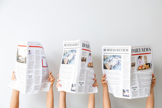 Female hands with newspapers on light background